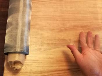 A roll of high transmittance stainless steel wire mesh on a yellow wooden table.
