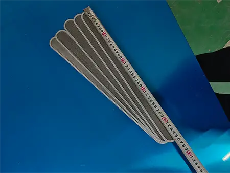 Five long strip edge stainless steel filter pieces on a blue table measuring length